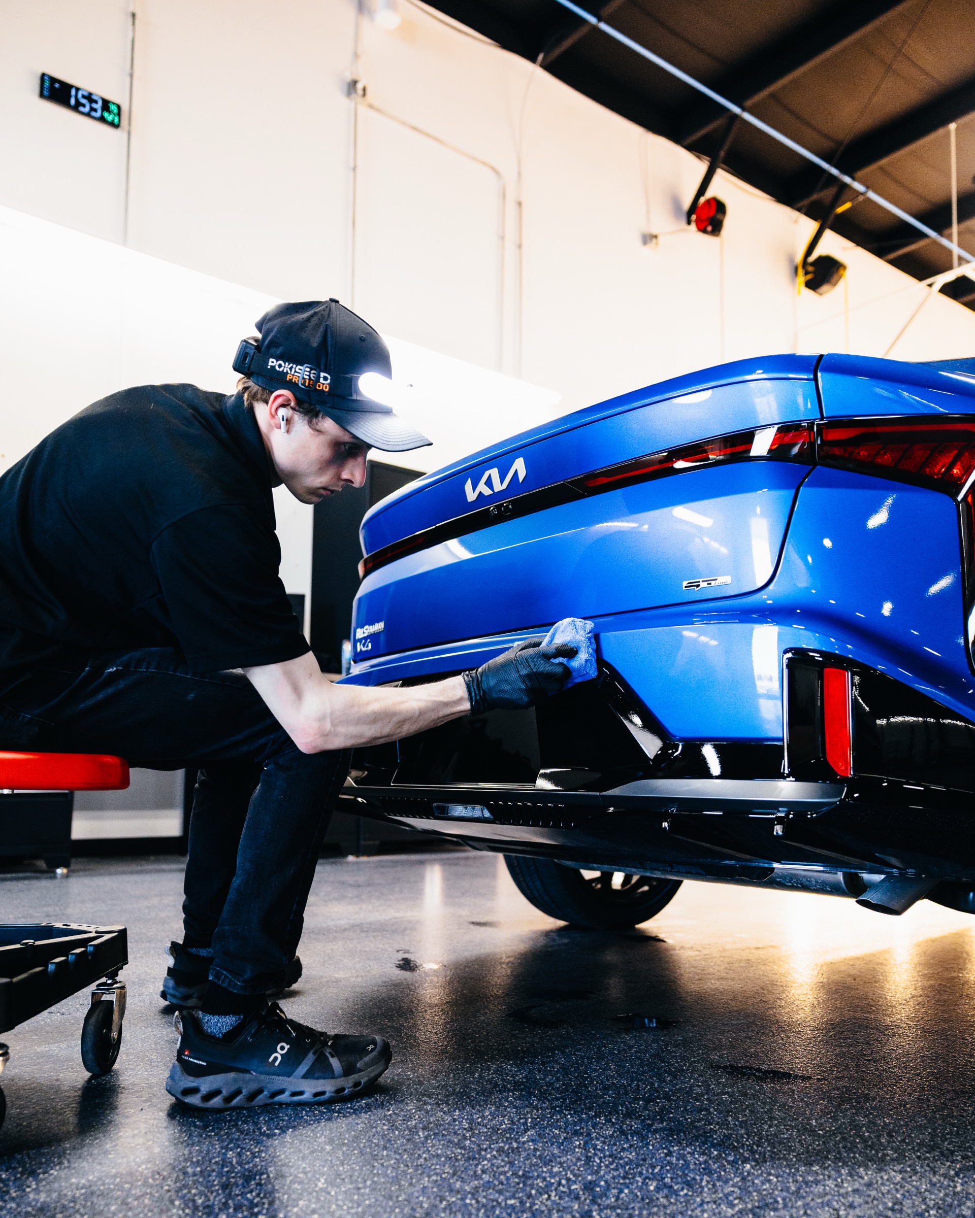 Technician detailing the rear bumper of a blue Kia at Pristine Film Solutions